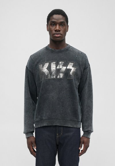 Sweatshirt gris foncé avec une finition délavée, arborant un logo métallique "KISS" rehaussé de clous. Col rond classique et poignets côtelés.