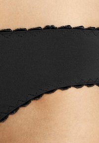 Fascia di biancheria intima nera con bordo ondulato e cuciture decorative, realizzata in materiale morbido, che mostra una texture delicata e linee pulite.
