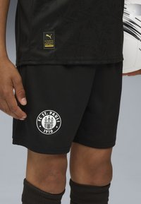 Svarta fotbollsshorts av andningsbart material, med en vit FC St. Pauli-logga och en liten guld Puma-tagg på nederkanten.