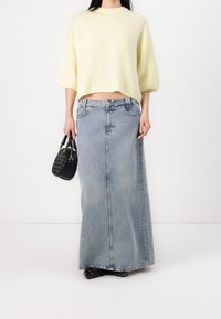 Helles gelbes, kurzärmliges Sweater kombiniert mit einem langen, blauen Jeansrock und einer kleinen schwarzen Handtasche mit strukturierter Oberfläche und doppelten Griffen.
