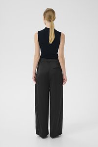 Schwarze hochgeschnittene Hose mit weitem Bein, glattem Stoff und einer Detailtasche auf der Rückseite. Tragen Sie dazu ein eng anliegendes, ärmelloses Oberteil in Marineblau.