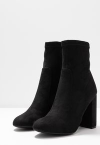 Schwarze Wildleder-Stiefeletten mit hohem Blockabsatz, runder Zehenpartie und nahtlosem Design. Verfügt über seitliche Einsätze und eine glatte Textur.