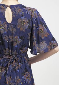 Navy floral dress with short flutter sleeves, featuring multicolored floral patterns, a tie belt at the waist, and a keyhole back detail.