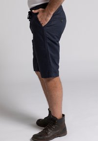 Pantalones cortos azul marino con cintura elástica, bolsillos laterales y detalles de botones. Combinados con botas de cordones marrón oscuro.