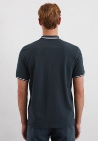Tmavě zelené polo tričko s úzkým střihem, krátkými rukávy a bílým lemováním límce a manžet. Hladká bavlněná tkanina, minimalistický design.