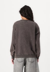 Oversized gray sweatshirt with a worn texture, ribbed cuffs and hem, and a crew neckline, paired with high-waisted gray denim jeans.