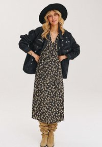 Černé květinové zavinovací šaty se béžovými a bílými vzory, doplněné černou džínovou bundou a béžovými řasenými kozačkami ke kolenům. Černý klobouk s širokým kremplem.