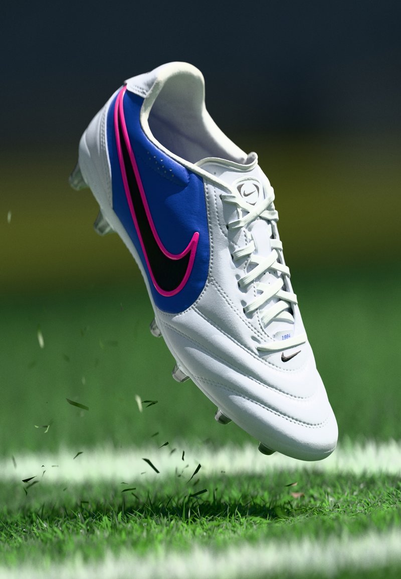 Ποδοσφαιρικό παπούτσι Nike σε λευκό, μπλε και μαύρο με ροζ λεπτομέρειες, με συνθετικό επά νω μέρος, δέσιμο με κορδόνια και αγκράφες για πρόσφυση.