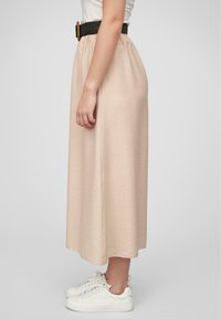 Jupe midi beige avec taille froncée, tissu texturé et ceinture tissée noire.Associée à des baskets blanches. Vue latérale, lignes fluides.