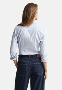 Světle modrá košile na knoflíky s vyhrnutými rukávy, doplněná tmavě modrými džínami s dvěma zadními kapsami a hnědým koženým opaskem.