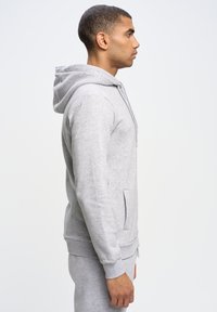 Sudadera gris con capucha ajustable, bolsillo frontal y puños acanalados. Hecha de tejido suave, presenta un corte relajado. Sin patrones ni acentos.