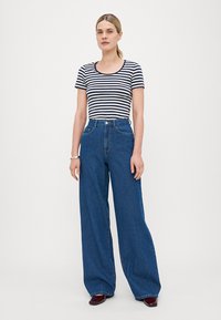 Striped short-sleeve t-shirt paired with high-waisted, wide-leg blue denim jeans. Smooth texture, with prominent stitching and a button closure.