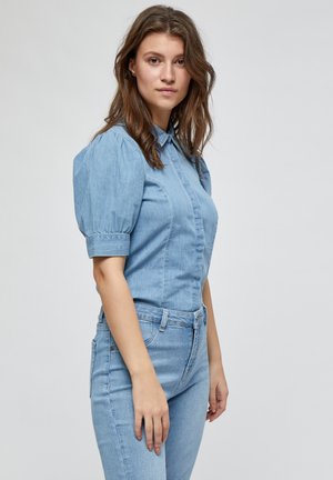 Lichtblauw denim overhemd met puffmouwen, kraag, verticale naden en knoopsluitingen, gedragen met bijpassende slim-fit jeans.