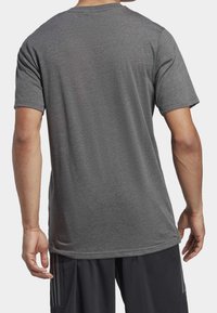 Camiseta gris de manga corta con cuello redondo. Tela suave y texturizada; corte relajado; sin marcas ni patrones visibles. Diseño simple.