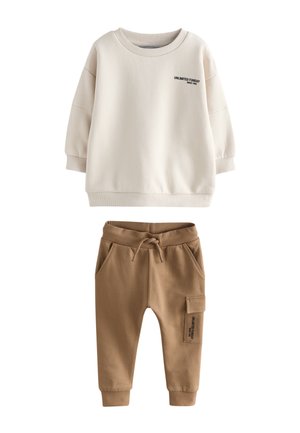 Krém színű hosszú ujjú pulóver „Unlimited Funday” felirattal és világosbarna jogger nadrág zsinórral és oldalzsebbel egyszínű háttéren.