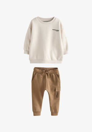 Beżowe i białe sneakersy z brązowymi akcentami, z teksturowaną gumową podeszwą, sznurowanym zapięciem oraz perforacjami na palcach.