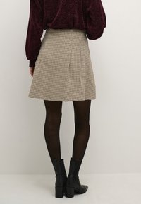 Jupe plissée à motif vichy beige et noir, dotée d'une taille ajustée et d'un ourlet évasé. Associée à des bottines noires et des collants.