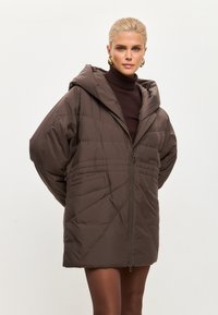 Pufferjack in donkerbruin, met een capuchon, ritssluiting en diagonale quilting. Inclusief zijzakken, ruime mouwen en een ontspannen pasvorm.