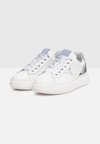 Des baskets blanches présentent une tige en cuir lisse, des accents bleu clair sur la languette et le talon, ainsi qu'une épaisse semelle en caoutchouc blanc avec un motif texturé.