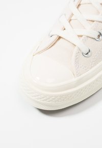 Sneaker in tela beige con suola in gomma texturizzata, punta rotonda, lacci bianchi e occhielli argentati. Design semplice con accenti lisci.