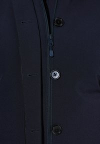 Chaqueta navy de cremallera con textura suave, grandes botones negros, cierre central de cremallera y un pequeño detalle de lazo en el lado izquierdo.