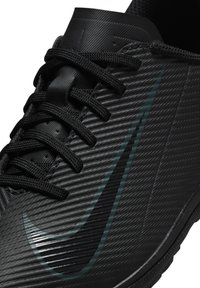 Scarpa sportiva nera con upper texturizzato, lacci neri e un logo Nike verde scuro. Presenta una suola liscia e un motivo a coste.