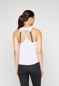 Bijela atletska majica s polu-prilagođenim oblikom, koja ima izrezani dizajn na leđima i crne Nike Pro trake. Glatka tekstura, minimalistički stil.