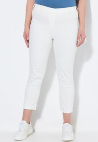 Pantalones blancos ajustados de tela texturizada, con una cintura ceñida y bolsillos laterales, combinados con zapatillas blancas.