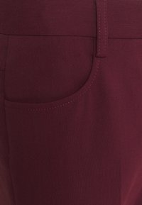 Burgundy kalhoty s hladkým texture, se boční kapsou a kontrastním prošitím. Vyrobené z odolné látky pro každodenní nošení.