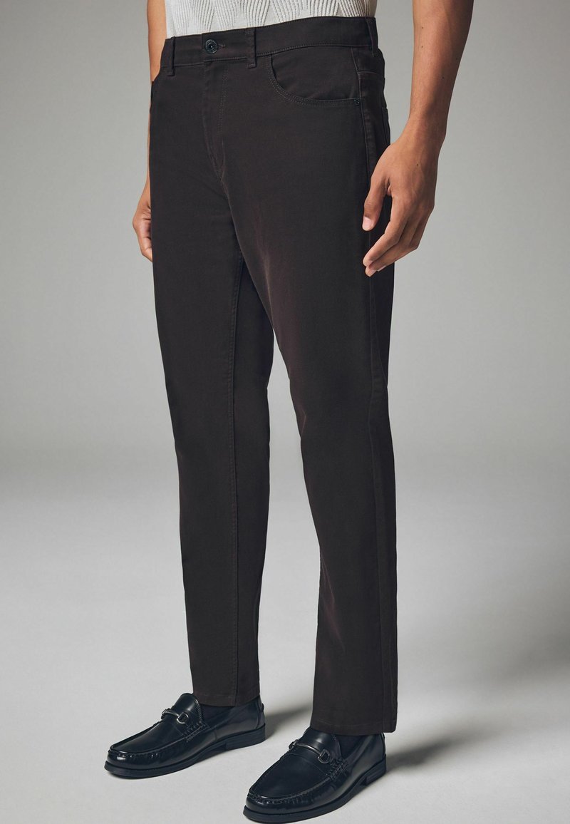 Dark brown pants with a smooth texture, slim fit, five-pocket design, and single button closure, paired with black loafers.