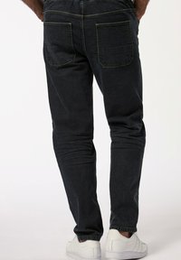 Vaqueros de mezclilla azul oscuro con corte ajustado, que cuentan con dos bolsillos traseros y sutiles detalles de costura, combinados con zapatillas blancas.