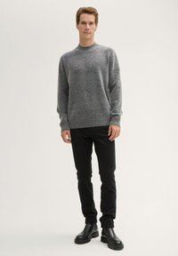 Grauer Strickpullover mit Rundhalsausschnitt, lässiger Passform, gerippten Bündchen und Saum, kombiniert mit schlanken schwarzen Hosen und schwarzen Stiefeletten.