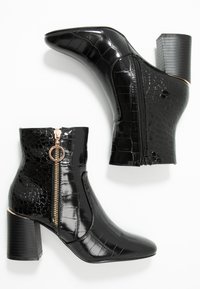 Svarta ankelstövlar med en glänsande krokodilmönster, med en sidoglasyr med en guldaccent och en blockklack. Slät yta, spetsig tå.