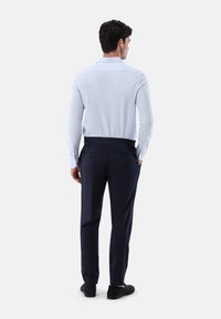 Helles blaues Langarmhemd, tailliert geschnitten mit einem Kentkragen, kombiniert mit dunklen marineblauen Hosen mit Seitentaschen und Gürtelschlaufen.