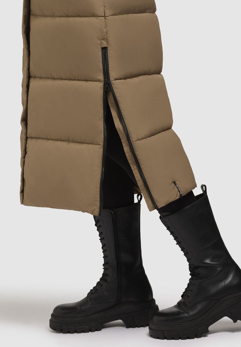 Puffy beige bovenkleding met een diagonale rits, gecombineerd met hoge zwarte leren laarzen met een dikke zool en vetersluiting.