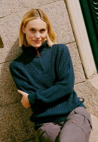 Marineblauwe gebreide pullover met een halve rits, geribbelde halslijn en textuurpatroon. Kenmerkt een zijknopaccent en een relaxte pasvorm.