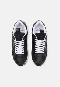 Black athletic shoes made of leather and mesh; features white laces, padded collar, and logo on the tongue and side.