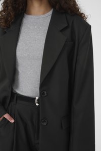 Blazer negru croiuit, cu doi nasturi, revere ascuțite, asortat cu un tricou gri deschis cu dungi fine. Material elegant și design structurat.
