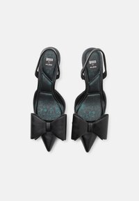 Black pointed-toe slingback heels with a large bow detail at the front. Smooth leather material with a patterned interior in teal and black.