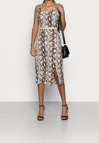 Midiklänning med ett ormtryck i beige och svart, med ett bälte i midjan, djup V-ringning och en slits fram. Matchas med svarta sandaler med remmar.