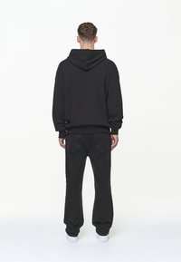 Svart huva-tröja med avslappnad passform, ribbade mudd och midjeband, tillsammans med lösa svarta jeans och vita sneakers.