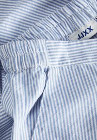 Randigt tyg i ljusblått och vitt, med ett elastiskt midjeband och en etikett som visar "JJXX" på den övre kanten.