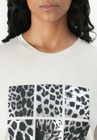 Light beige t-shirt with a round neckline featuring a six-panel leopard print design in black and silver textures.