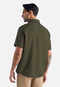 Korte mouw shirt in olijfgroen, gemaakt van een gladde stof. Kenmerkt zich door een puntige kraag en een ontspannen pasvorm met subtiele stiksels.