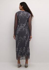 Duga, siva haljina s prozirnim dugim rukavima, ukrašena šljokičastim cvjetnim uzorcima. Tekstura tkanine se proteže do polu-listova s ravnim rubom.