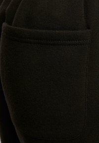 Gros plan sur une poche en tissu noir avec des coutures détaillées sur un vêtement.