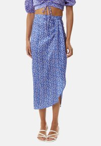 Blue patterned wrap skirt with a high slit, made of a lightweight fabric. The design features abstract shapes in varying shades of blue.
