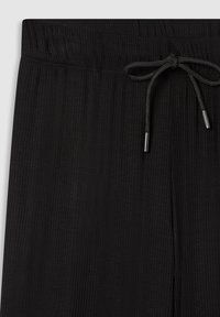 Pantaloni neri realizzati in un materiale a coste e texturizzato. Hanno una vita elasticizzata con cordoncino e terminali in metallo.
