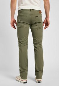 Pantalones de algodón verdes con corte recto, que presentan bolsillos traseros, detalles de costura sutiles y un parche de logo de cuero marrón en la cintura.