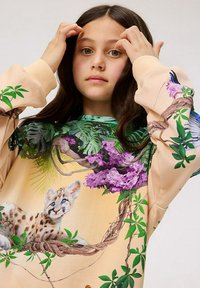 Sweatshirt features an artistic design with a lounging snow leopard, purple flowers, and green foliage on a beige background. Long sleeves.